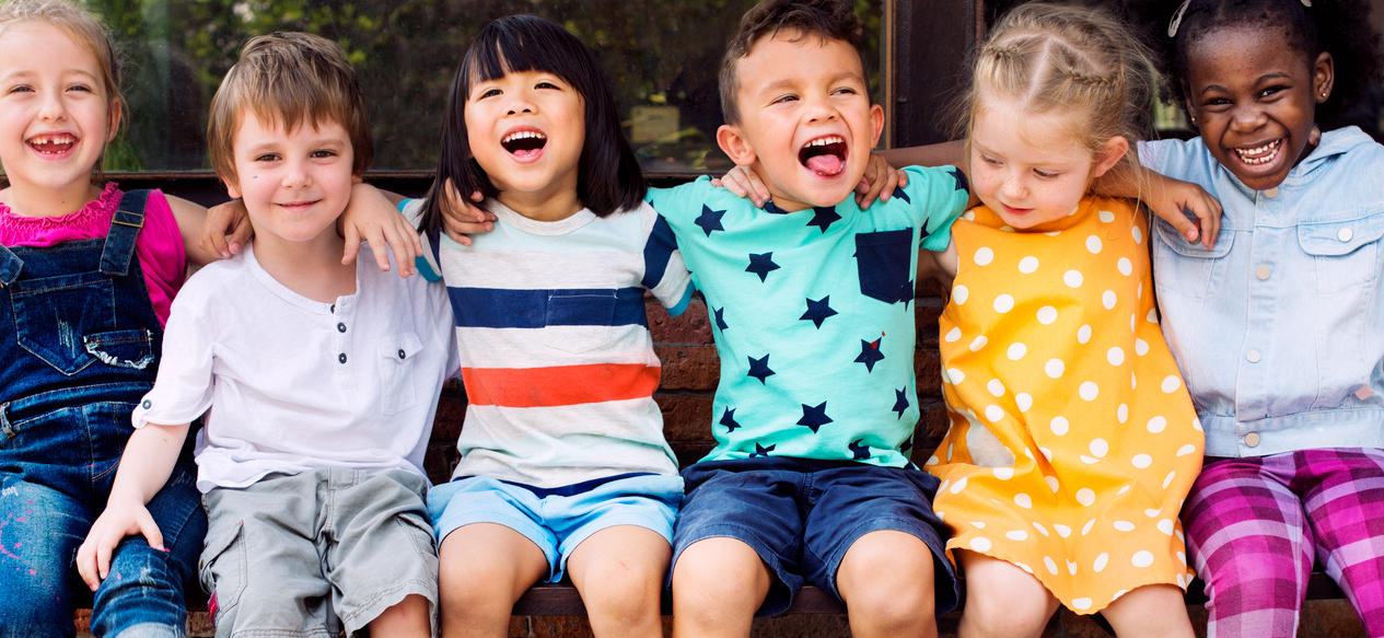 Six children sitting on a bench together, laughing