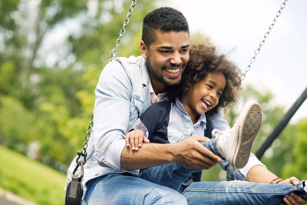 Parents swinging a child by the hands in a sunlit field